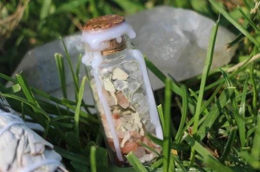 Crystal ritual jar with cork and herbs on grass, white wax dripped, next to a quartz crystal