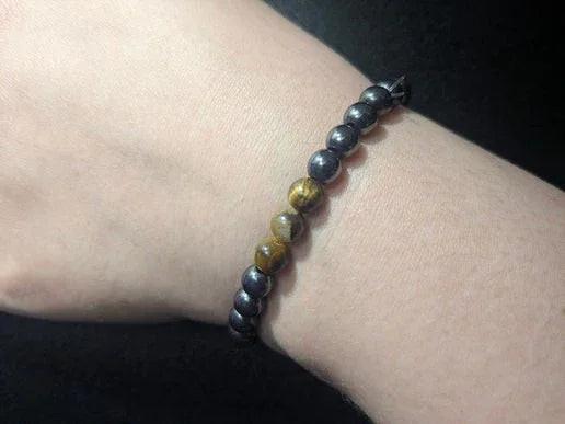 Hand wearing a crystal bead bracelet with tiger's eye and black beads, against a dark background.