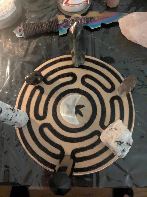 Crystal grid with moon symbols, black labyrinth design, assorted crystals, and ritual knife