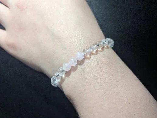 Hand wearing a clear quartz and rose quartz crystal bead bracelet on black background