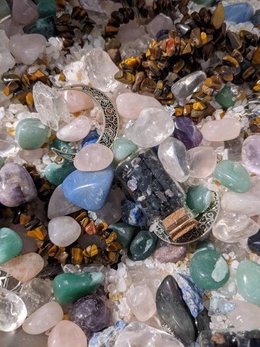 Assorted crystals and gemstones with crescent moon jewelry and a small corked vial